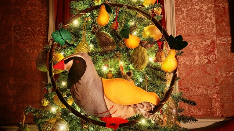 A textile bird sits in a Christmas tree surrounded by crochet and glass baubles and twinkly lights.